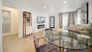 A modern living room with a glass dining table, a sofa, a TV, and a fireplace.