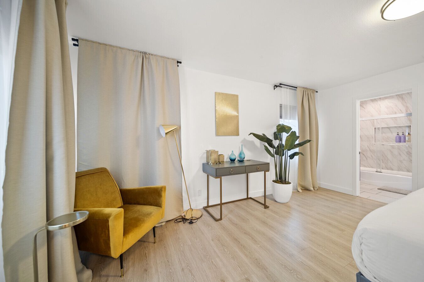 A hotel room with a yellow armchair, a small table with decorative items, a potted plant, and a shower area with shelves.