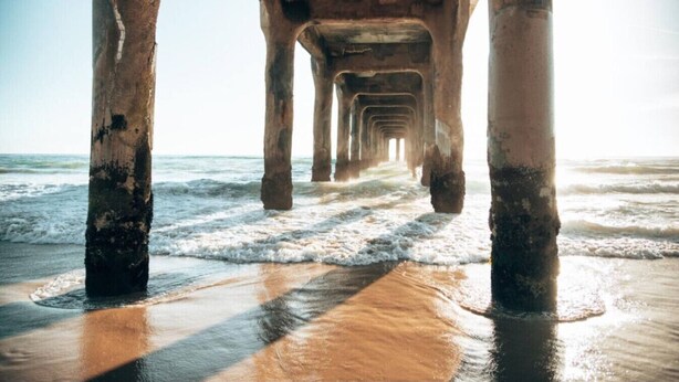 A pier extending into the ocean with visible wooden supports and waves crashing at the base.
