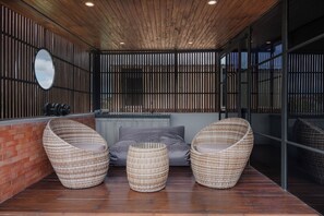 A modern outdoor seating area with wicker chairs and a small table, a brick wall, and a wooden ceiling.