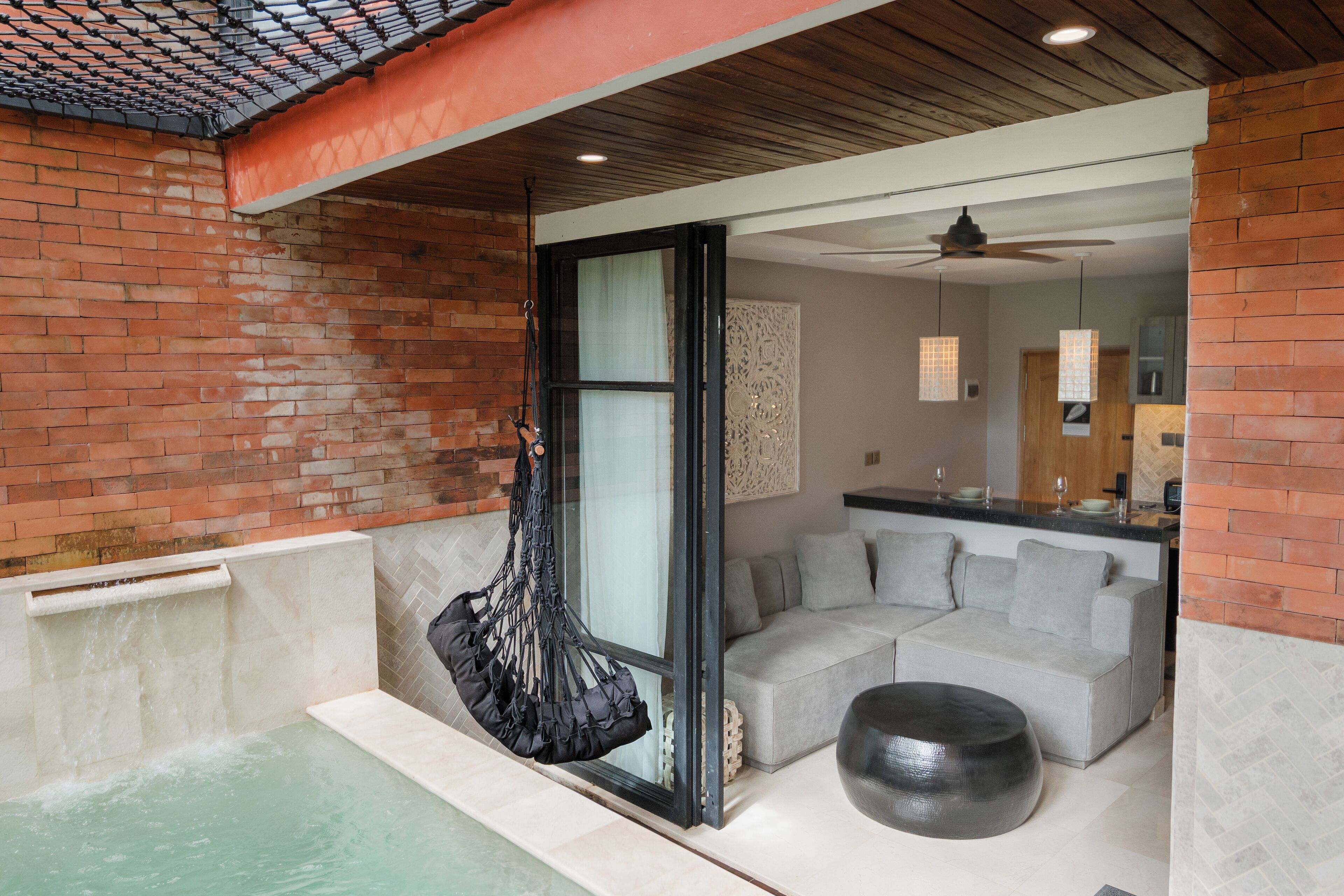 Un baño moderno con ducha de vidrio, una silla colgante y una zona de estar con sofá y reposapiés.