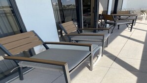 An outdoor seating area with modern chairs and tables, a glass door entrance, and a view of the surrounding area. - 1 bedroom plus STUDIO on Vanderbilt Beach. Beach access, water views. Sleeps 4 (Naples)