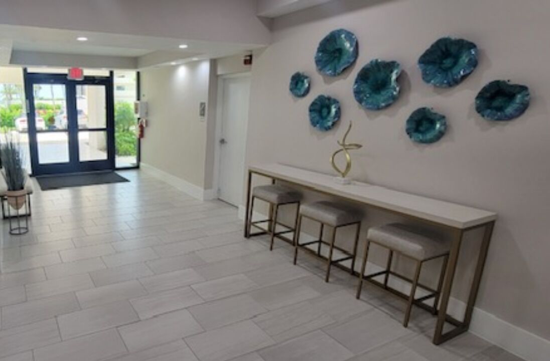 Un espace d’accueil avec un banc et des tabourets, un mur orné d’assiettes décoratives et une porte donnant sur l’extérieur.