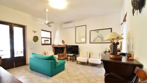 A living room with a teal sofa, white armchairs, a wooden coffee table, a TV, and a ceiling fan. - Cottage with a/c two bedrooms and two bathrooms (Aglientu)