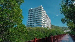 A modern high-rise hotel with multiple balconies, surrounded by lush greenery and a wooden walkway. - Charming seafront 2-bedroom apartment with AC, WiFi in delightful Santa Marta (Santa Marta)