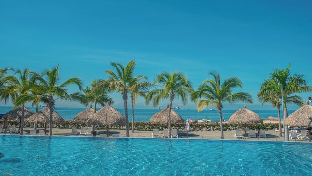 A clear blue pool with lounge chairs and palm trees, overlooking the ocean. - Charming seafront 2-bedroom apartment with AC, WiFi in delightful Santa Marta (Santa Marta)