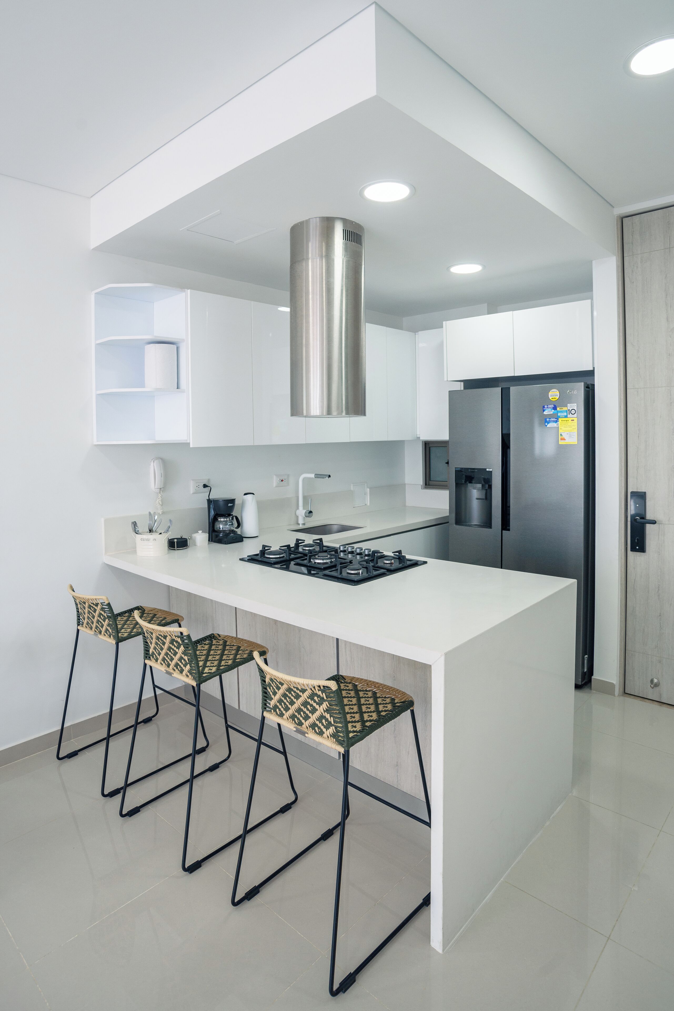 A modern kitchen with a central island, stainless steel appliances, and three woven chairs.
