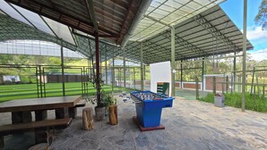 An indoor sports facility with a foosball table, benches, and a view of an outdoor field.