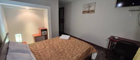 A hotel room with a bed, a desk, a chair, a television, and a painting on the wall.