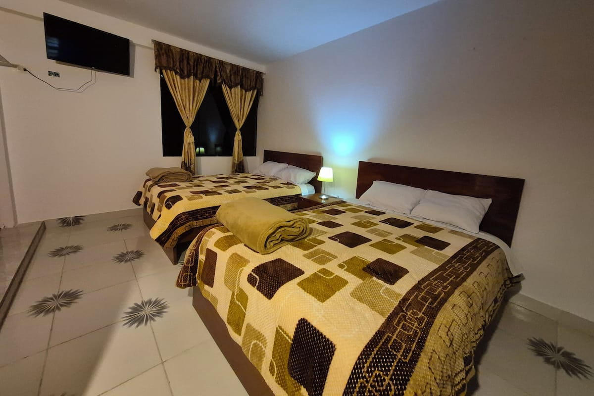 A hotel room with a large bed, a TV mounted on the wall, and a window with curtains.