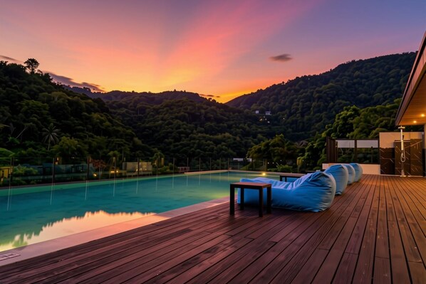 A wooden deck with a pool, lounge chairs, and a view of a forested hillside.