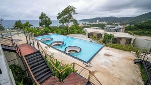 A rooftop pool with three hot tubs, surrounded by a concrete deck and stairs leading to a building. - Brand New 2 Bed Seaview Apartment Utopia Karon (karon)