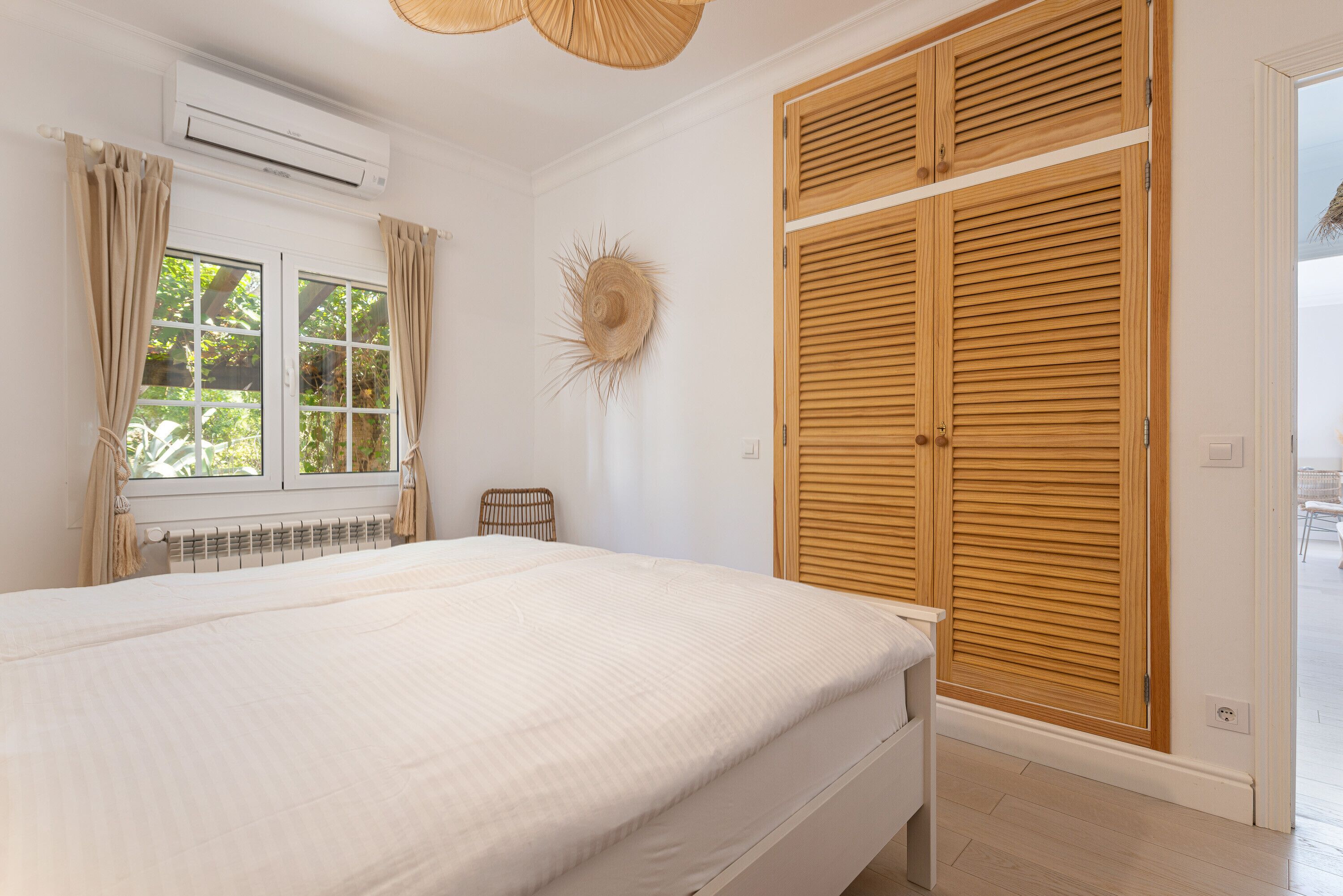 Ein Schlafzimmer mit Bett, einem fenster mit Vorhängen, einer Klimaanlage, einem Holzschrank und einem Wanddekor.