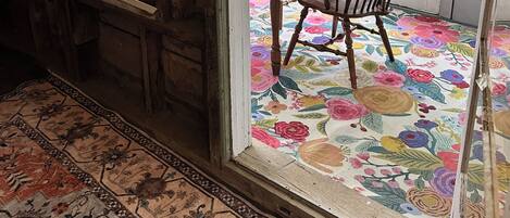 Une pièce avec une table et des chaises en bois, un tapis à motifs floraux et une vue sur un jardin verdoyant par les fenêtres.