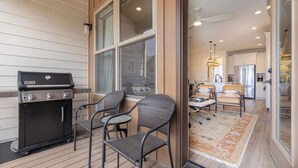A patio with a grill, two wicker chairs, and a view into a modern kitchen with a refrigerator and dining area.