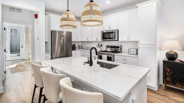 A modern kitchen with white cabinets, stainless steel appliances, a large island with bar stools, and two hanging wicker pendant lights.