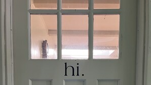 Une porte blanche avec une petite fenêtre et le mot « Salut » écrit au-dessus.