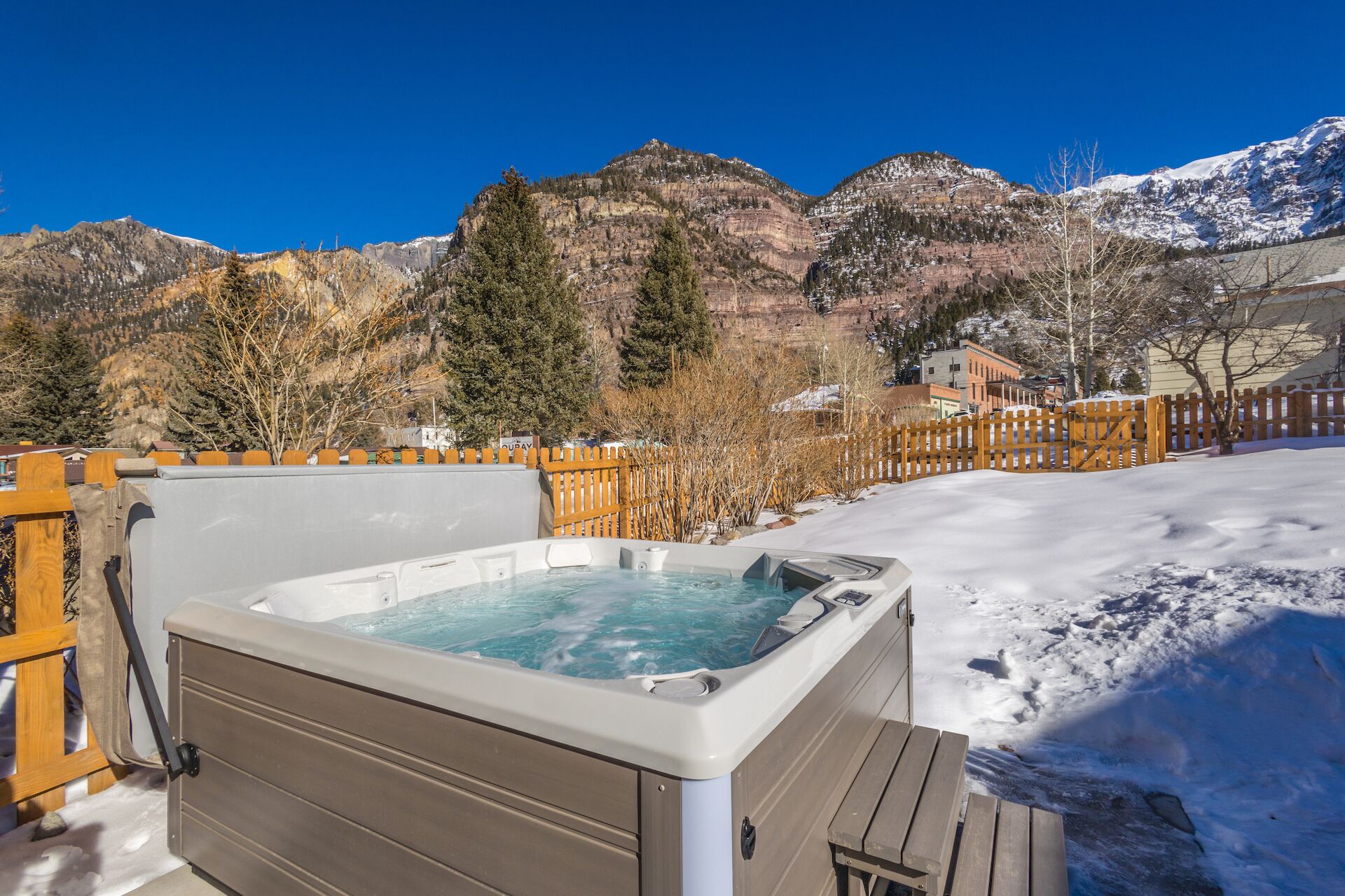 A hot tub with a wooden deck and a view of snow-covered mountains.