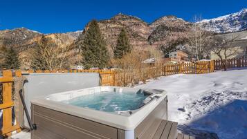 A hot tub with a wooden deck and a view of snow-covered mountains.