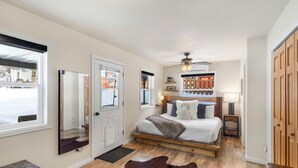 Een slaapkamer met een houten bed, een plafondventilator, een groot raam en een houten deur.
