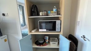 Een compacte kitchenette met een magnetron, een kleine koelkast en een plank met verschillende keukenspullen.