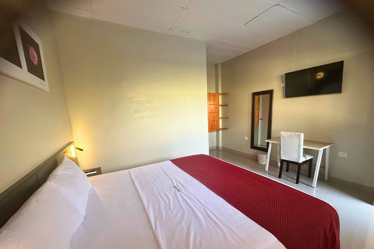 Ett hotellrum med en stor säng, ett skrivbord, en stol, en spegel och en tv på väggen.