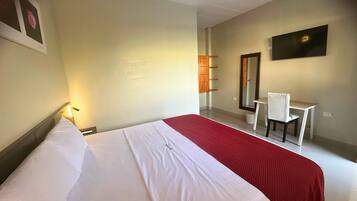 Habitación de hotel con una cama grande, un escritorio, una silla, un espejo y un televisor en la pared.