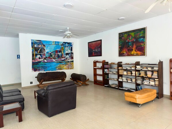 A spacious living room with a large painting of a cityscape, a bookshelf filled with books, and a modern ceiling fan.