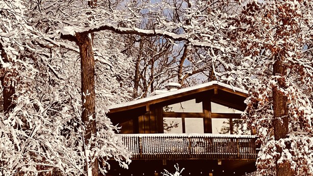 Una cabaña de madera con balcón, rodeada de árboles cubiertos de nieve.