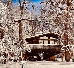A wooden cabin with a balcony, surrounded by snow-covered trees.