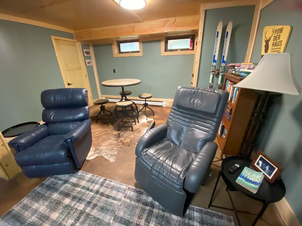 A cozy living room with two leather chairs, a small round table, a coffee table, and a bookshelf.