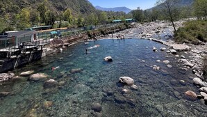 Un río cristalino con rocas, un muelle y un edificio con techo verde.