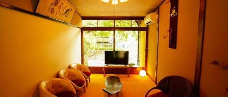 A cozy living room with a TV, a sofa, and chairs arranged around a central table.