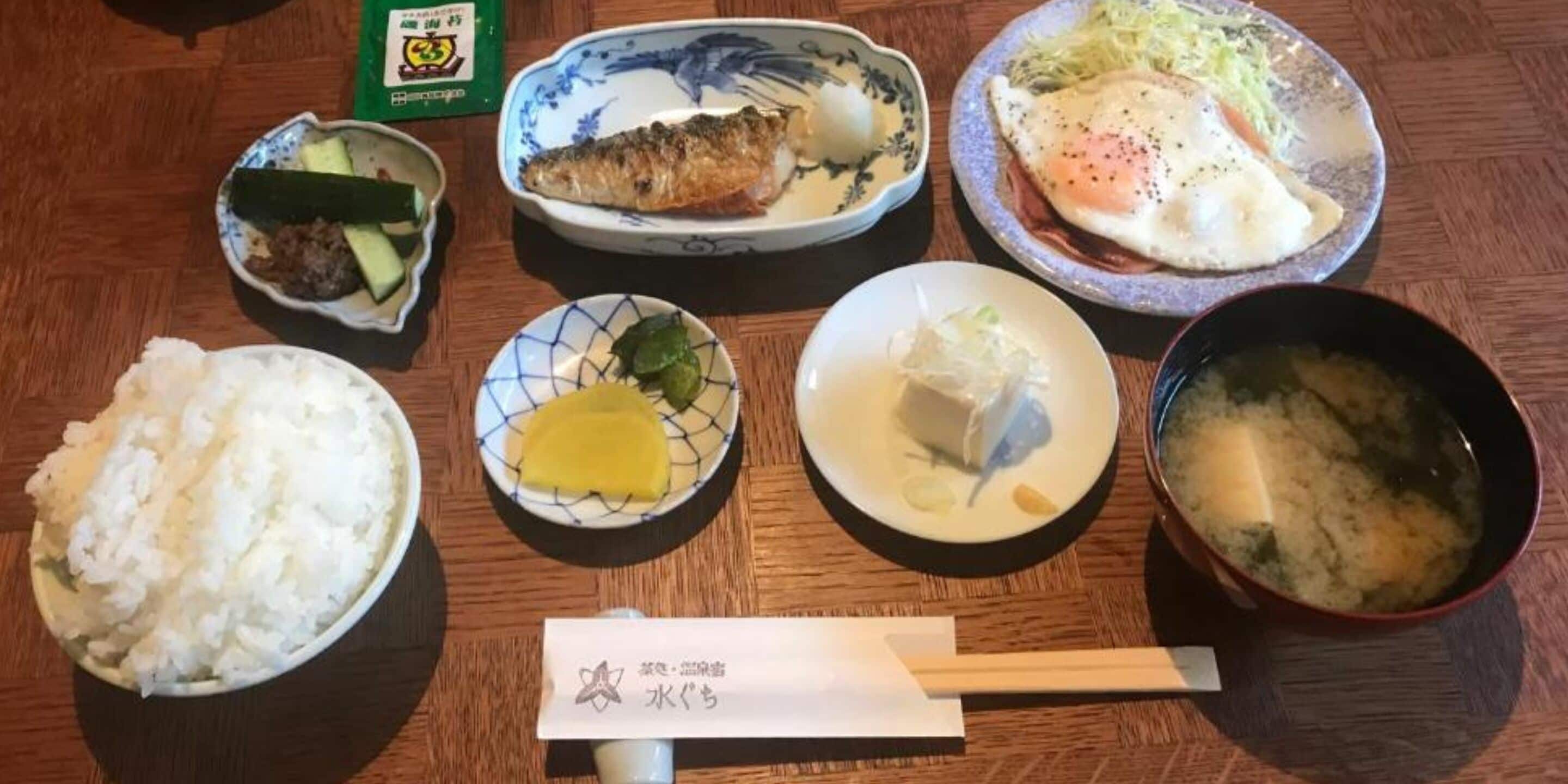 A wooden table with various dishes including rice, fish, vegetables, and soup.