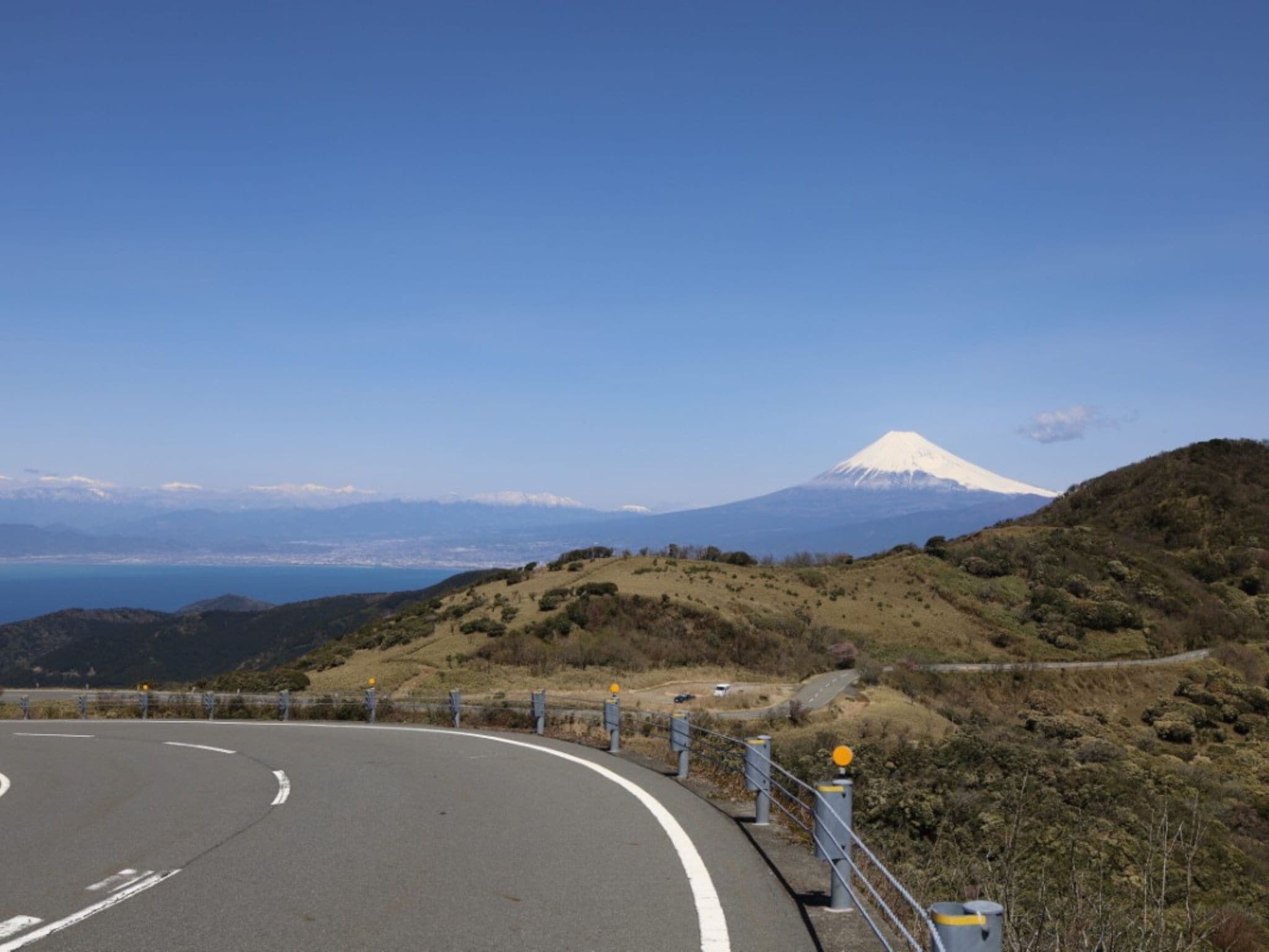 Una carretera sinuosa con barandillas, cielo despejado y una montaña nevada al fondo.