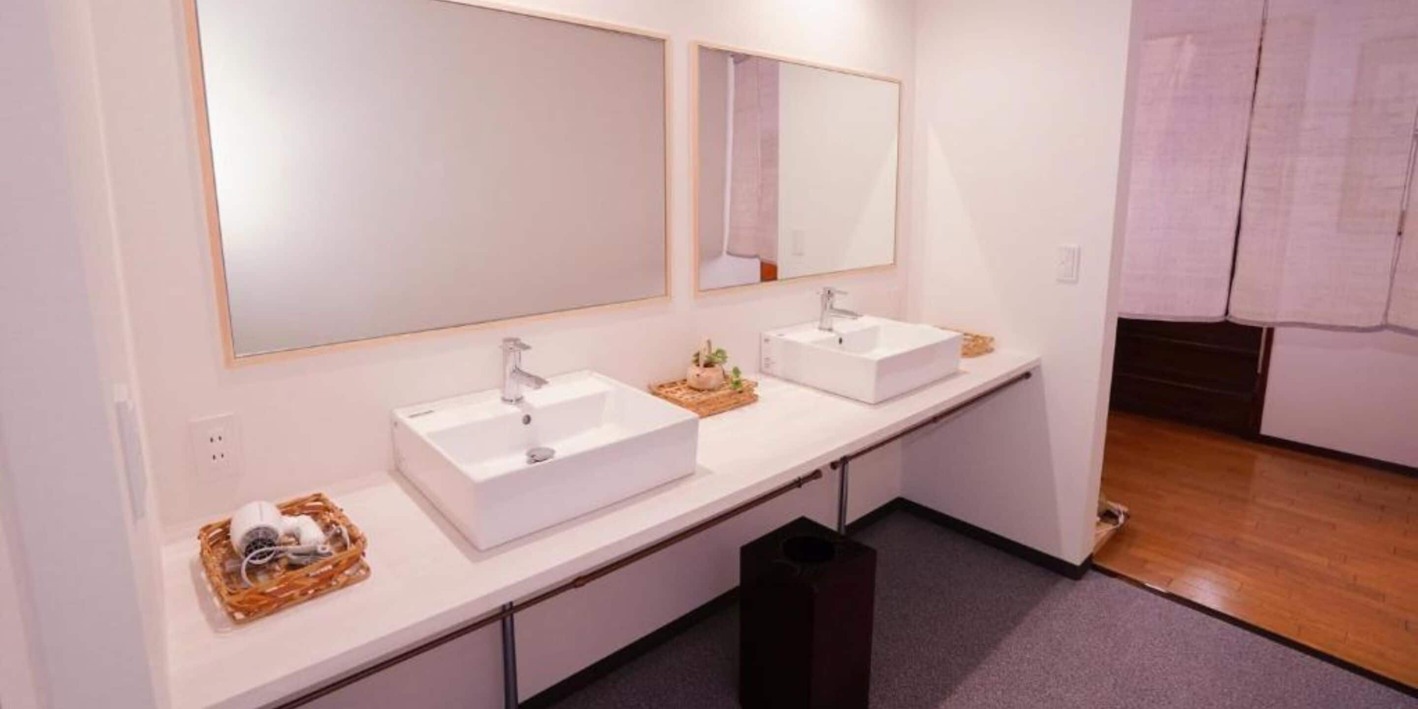 A modern bathroom with two white sinks, a large mirror above each, and a small plant on the countertop.