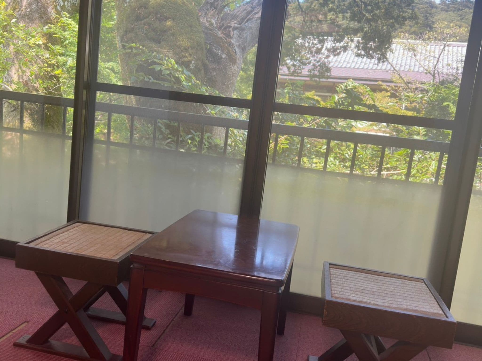 Una habitación con dos mesas de madera y un ventanal con vistas a follaje y un edificio.