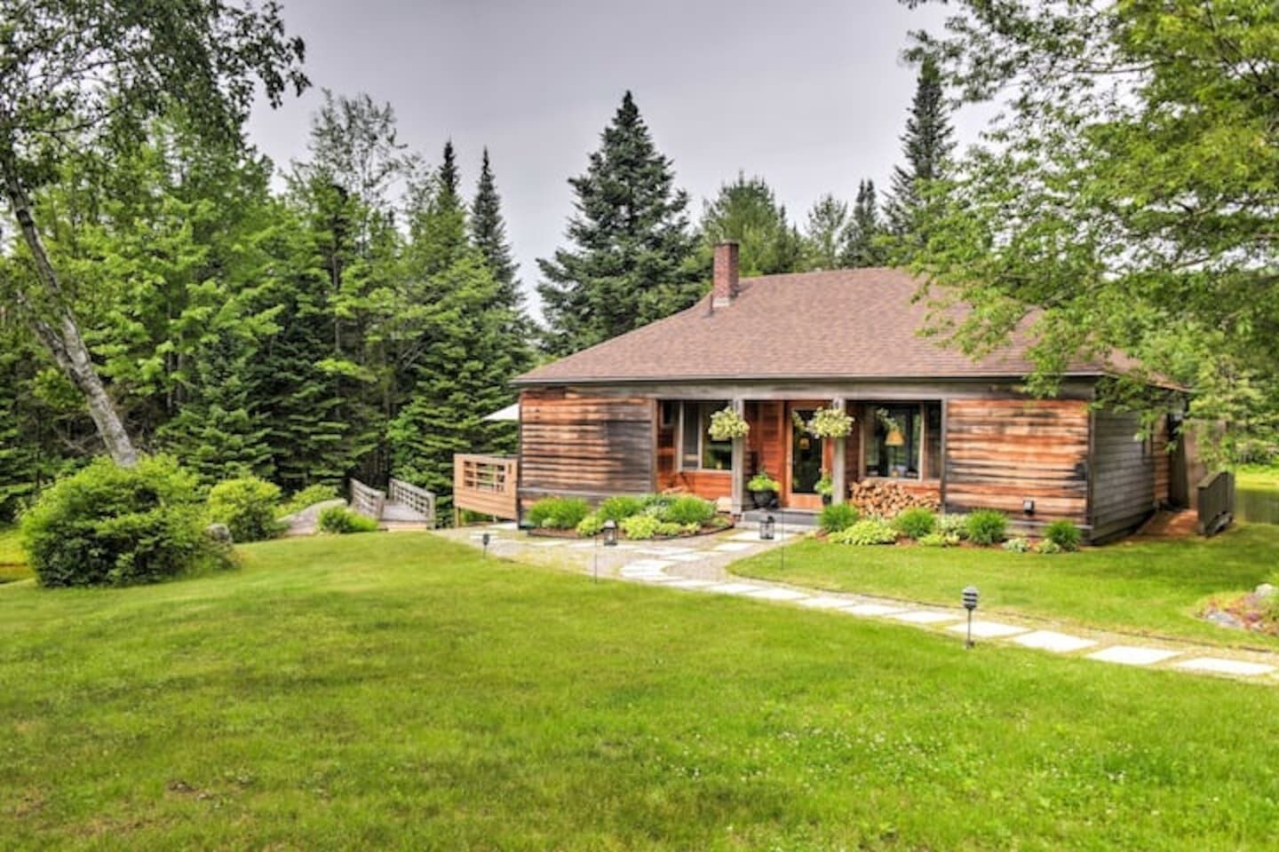Une cabane en rondins dotée d’un porche à l’avant, entourée d’une pelouse bien entretenue et d’une forêt dense.