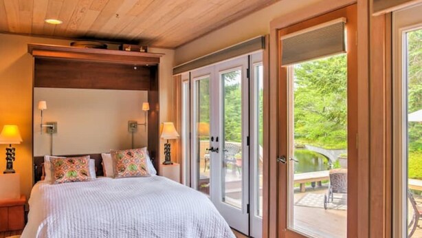 Een slaapkamer met een groot bed, twee bedlampen en uitzicht op een terras met tuinmeubels.