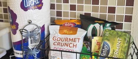 A kitchen counter with a roll of paper towels, a bag of gourmet crunch popcorn, a bag of Shiloh snacks, and a box of peppermint tea.