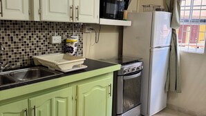 Una cocina con gabinetes verdes, una encimera negra, un microondas, una estufa y un refrigerador.