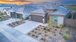 A modern residential area with houses featuring sloped roofs and solar panels, surrounded by landscaped gardens and a desert landscape.