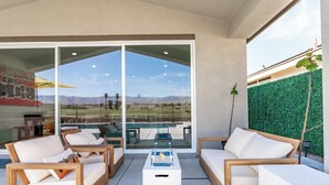 A modern outdoor seating area with white sofas and a coffee table, overlooking a scenic mountain view.