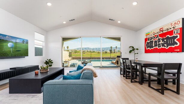 A spacious living room with a large window overlooking a pool and mountains, a dark wooden dining table, and a comfortable seating area.