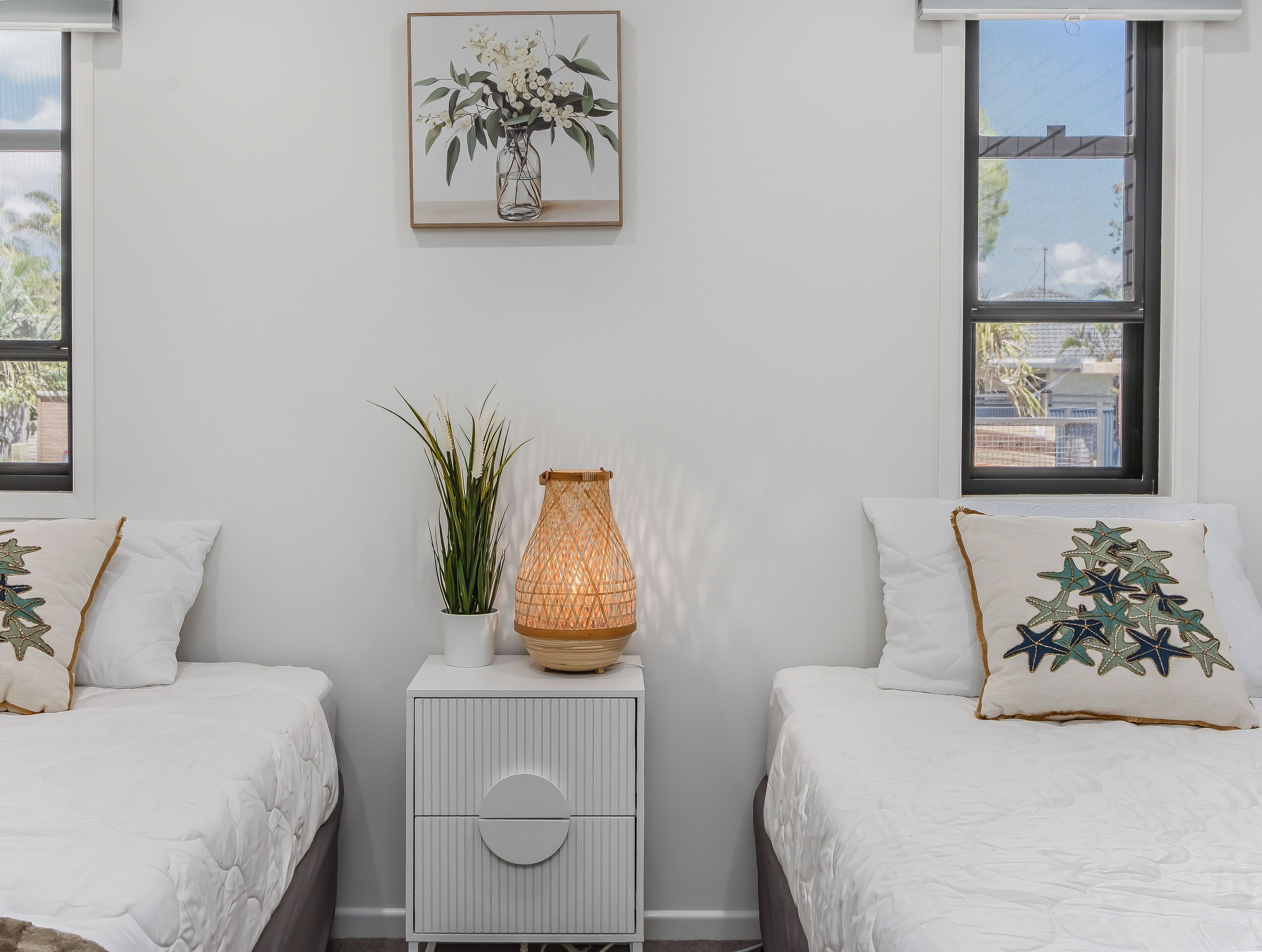 Ein Schlafzimmer mit zwei Betten, einem Nachttisch, einem Wandbild und einem Fenster.