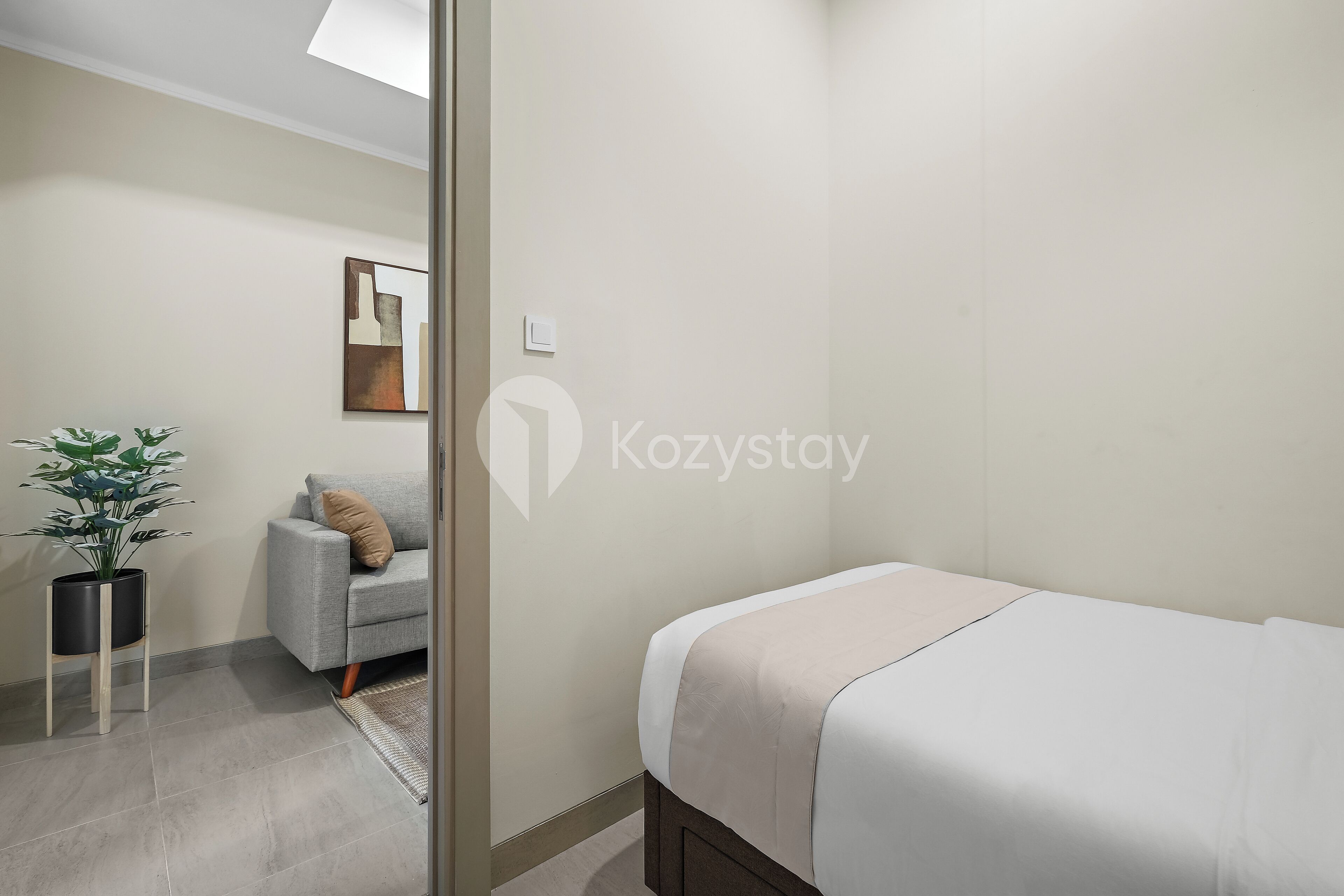 Een moderne slaapkamer met een bed, een grijze bank, een kleine potplant en een wanddecoratie.