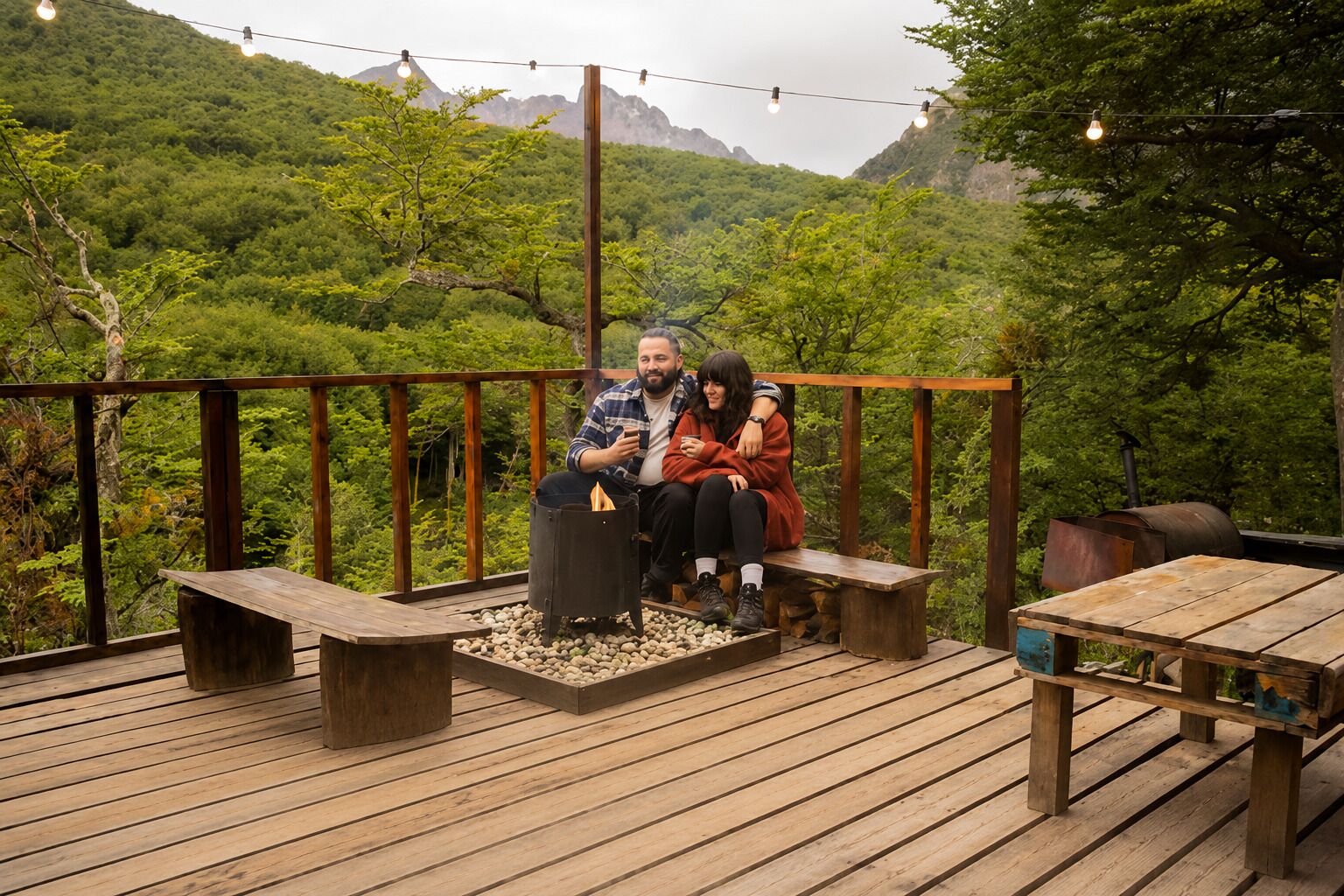 A couple sitting on a wooden deck with a fire pit, surrounded by lush greenery and mountains in the background.