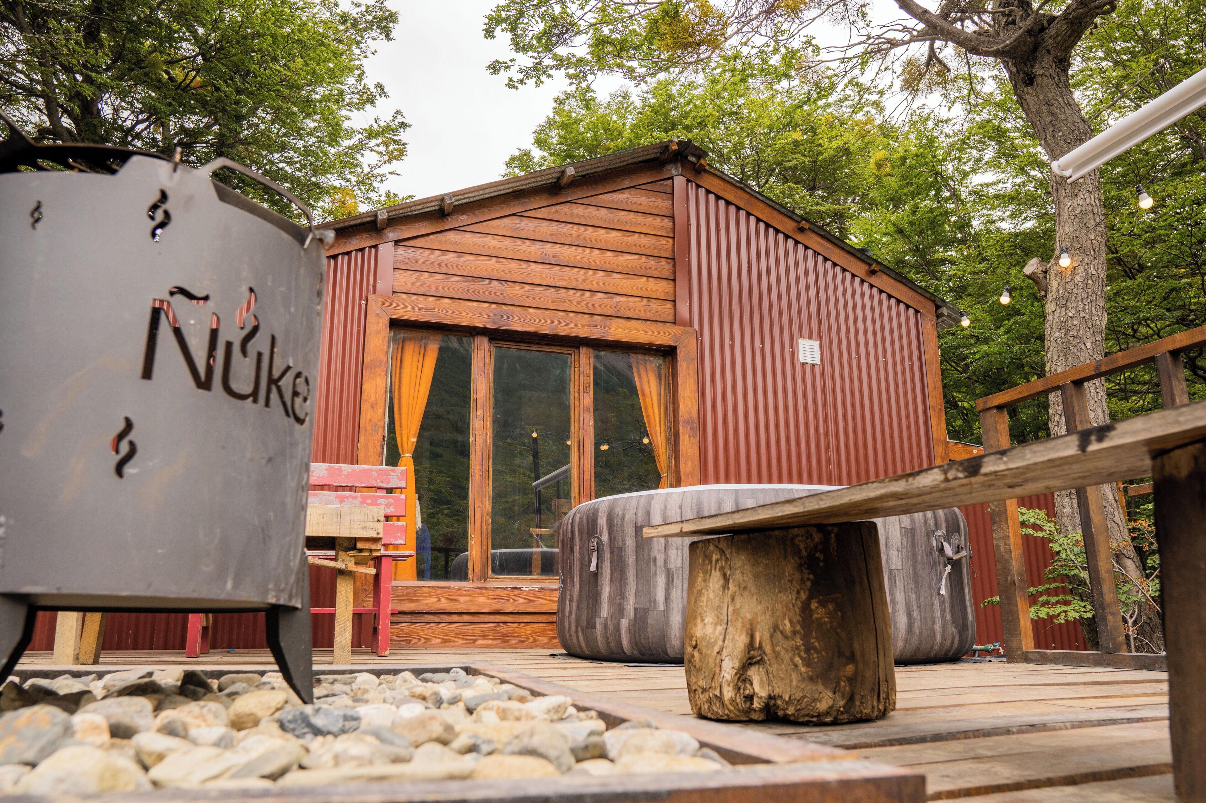 A rustic cabin with a wooden exterior, large windows, and a stone bench in the foreground.