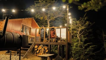 A rustic cabin with a wooden deck, a barbecue grill, and a string of lights.
