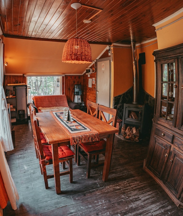 Una mesa de comedor de madera con cojines rojos, una lámpara colgante tejida y una chimenea rústica.